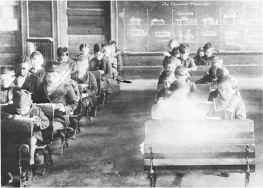 Old photo of a group of students sitting at thier desks. 